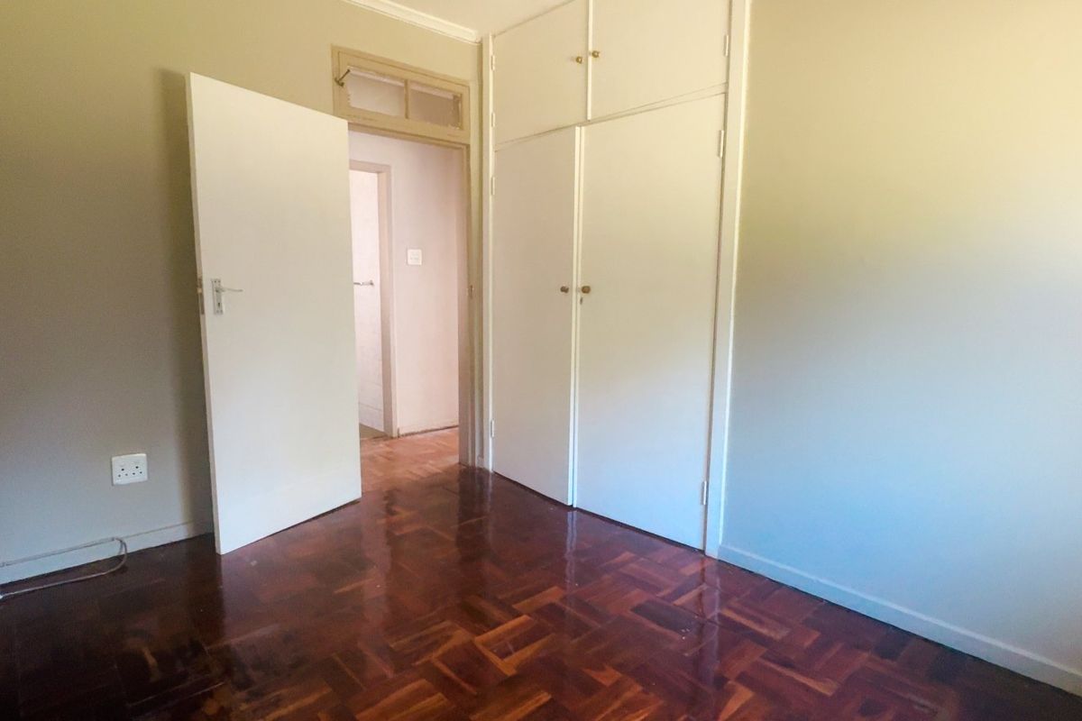 A bright, empty bedroom featuring polished parquet flooring and ample built-in cupboard storage with overhead compartments.