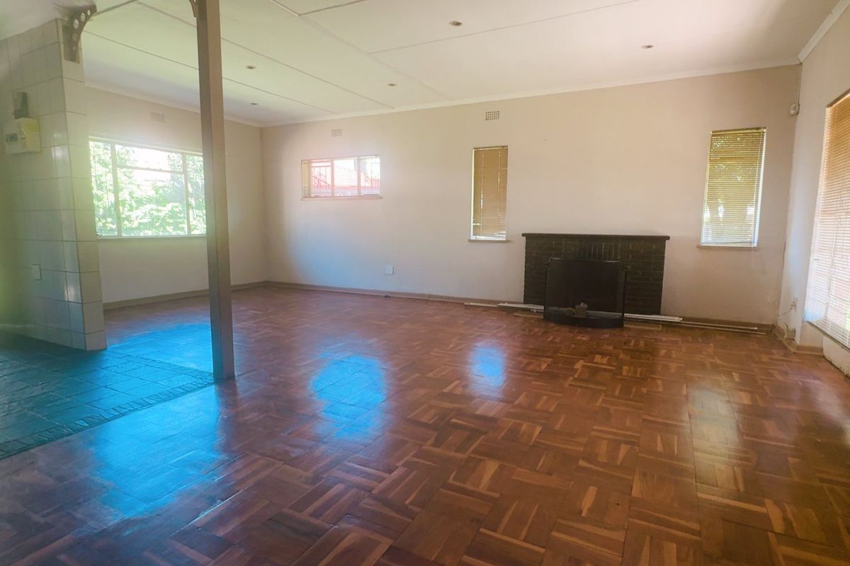 Spacious living area featuring classic parquet flooring, a brick fireplace, and large windows with fitted venetian blinds.