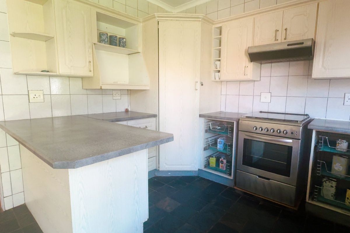 A functional kitchen featuring built-in cabinetry, laminate countertops, a tiled backsplash, and a freestanding oven with an extractor fan.