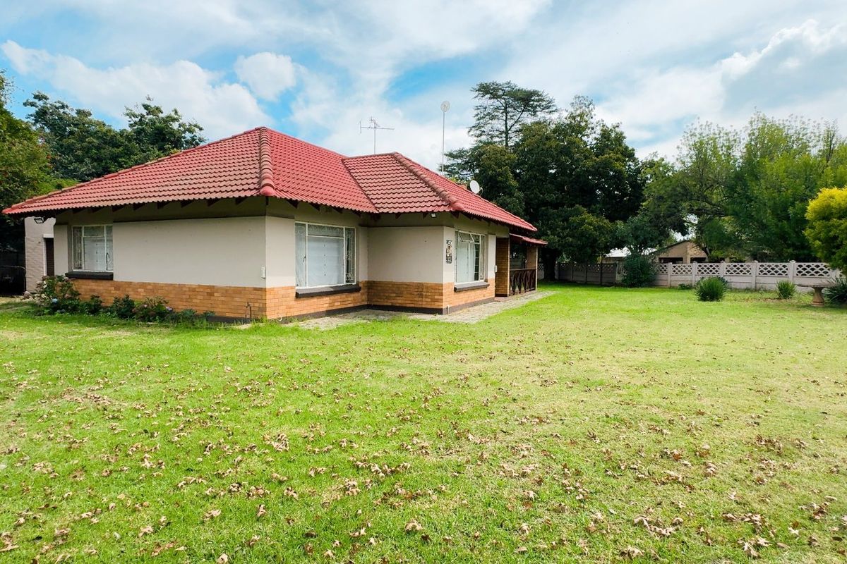 A view of the rear elevation of the house featuring a tiled roof, brick and plaster facade, and a spacious garden with boundary walling.