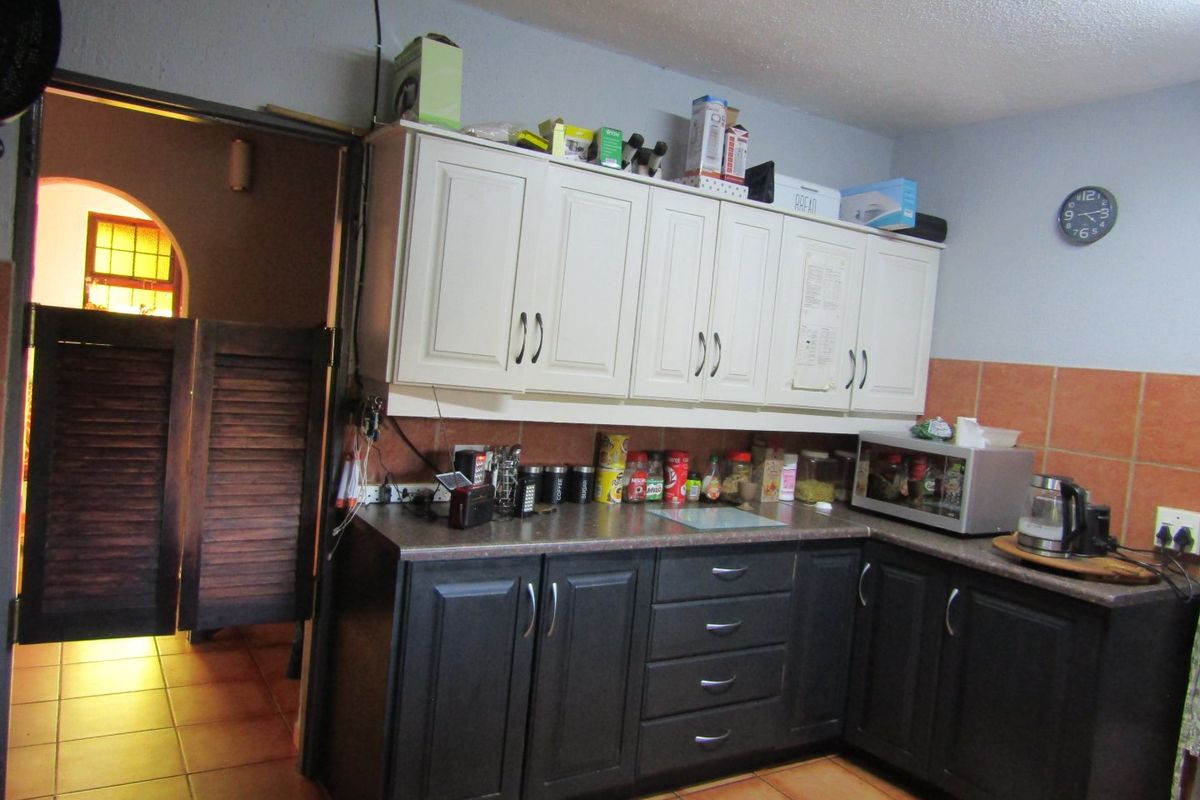 A functional kitchen featuring two-tone cabinetry, tiled backsplash, and terracotta-style floor tiles, with louvered doors leading to an adjacent room.