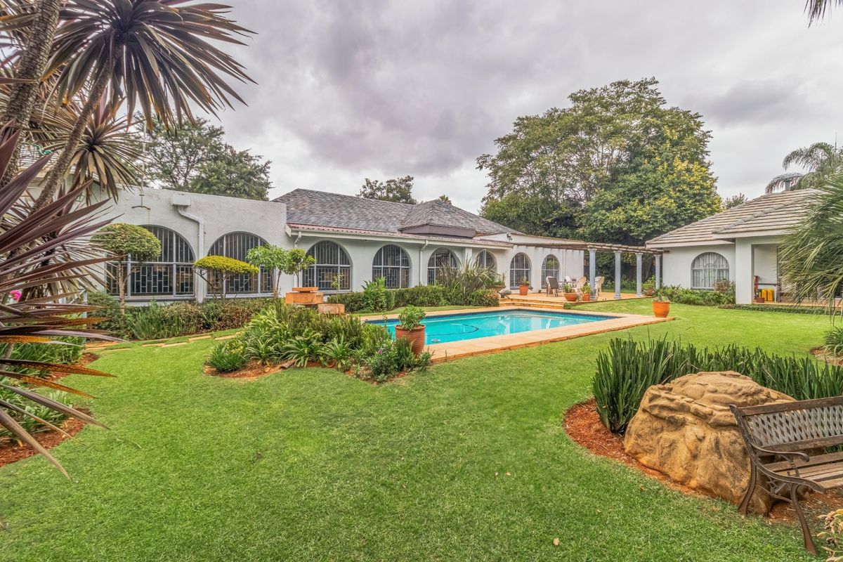 Spacious rear garden featuring a swimming pool, well-maintained lawn, and a paved patio area adjacent to the main house with arched window detailing.