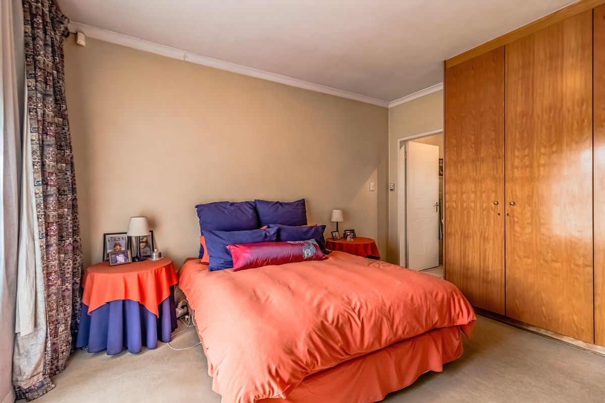 A bedroom featuring built-in wooden wardrobes, neutral wall finishes, and carpeted flooring, offering a functional space with potential for modern updates.