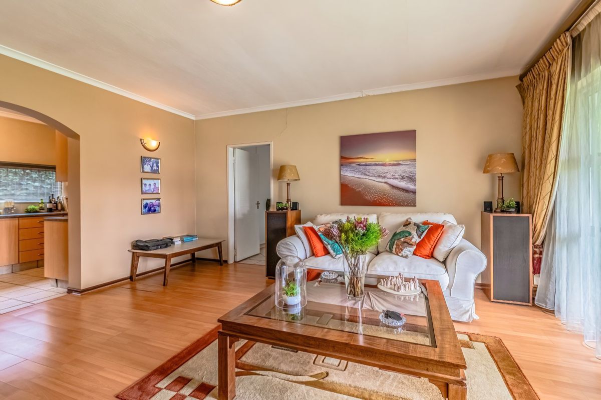 A comfortable living room featuring laminate flooring, coved ceilings, and an archway leading to the adjacent kitchen area.