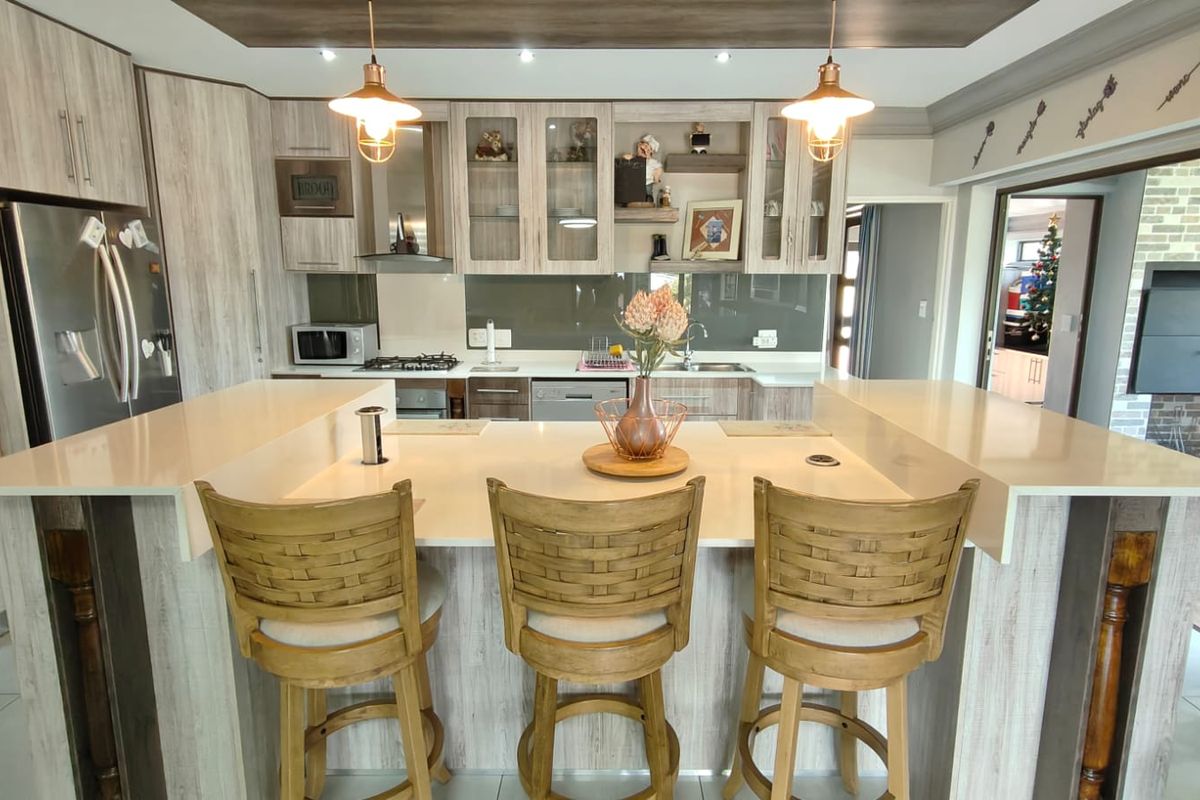 Modern kitchen featuring light wood-grain cabinetry, quartz countertops, a central breakfast island, and integrated appliances with stylish pendant lighting.