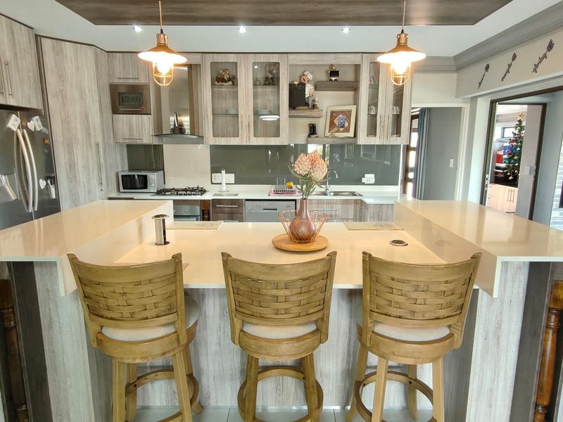 Modern kitchen featuring light wood-grain cabinetry, quartz countertops, a central breakfast island, and integrated appliances with stylish pendant lighting.