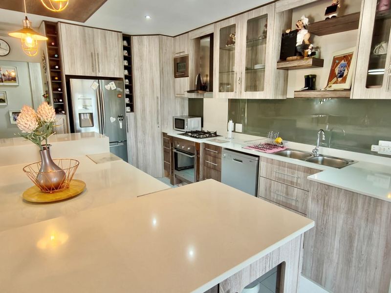Modern kitchen featuring light wood-grain cabinetry, stone countertops, glass splashback, and integrated appliances, including a gas hob and double sink.