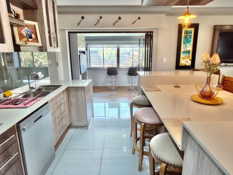 Modern open-plan kitchen featuring quartz countertops, sleek cabinetry, and a breakfast bar, seamlessly flowing into an adjacent living area with bi-fold doors.