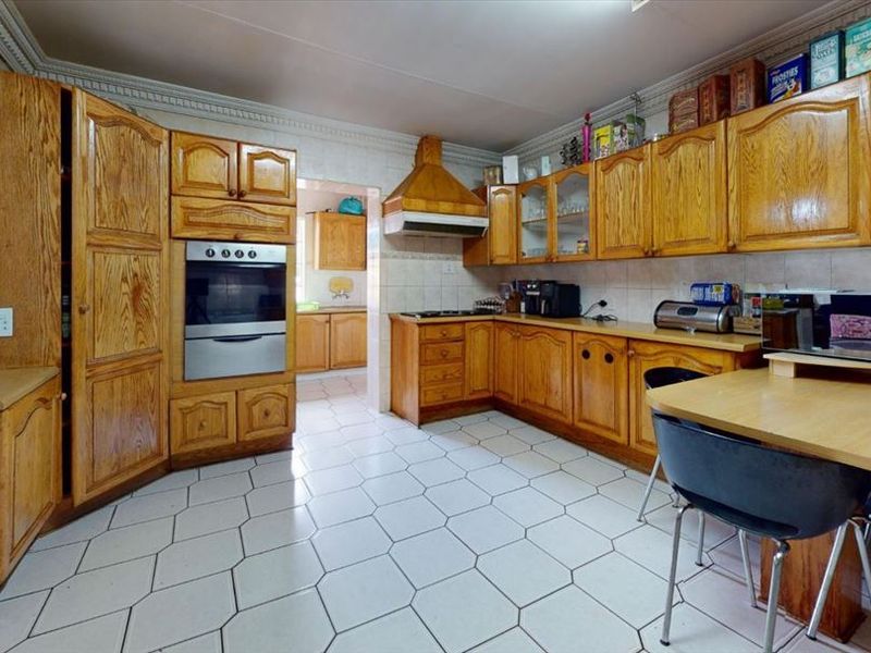 A functional kitchen featuring traditional wooden cabinetry, built-in oven, extractor fan, and tiled flooring, with an adjacent scullery area.