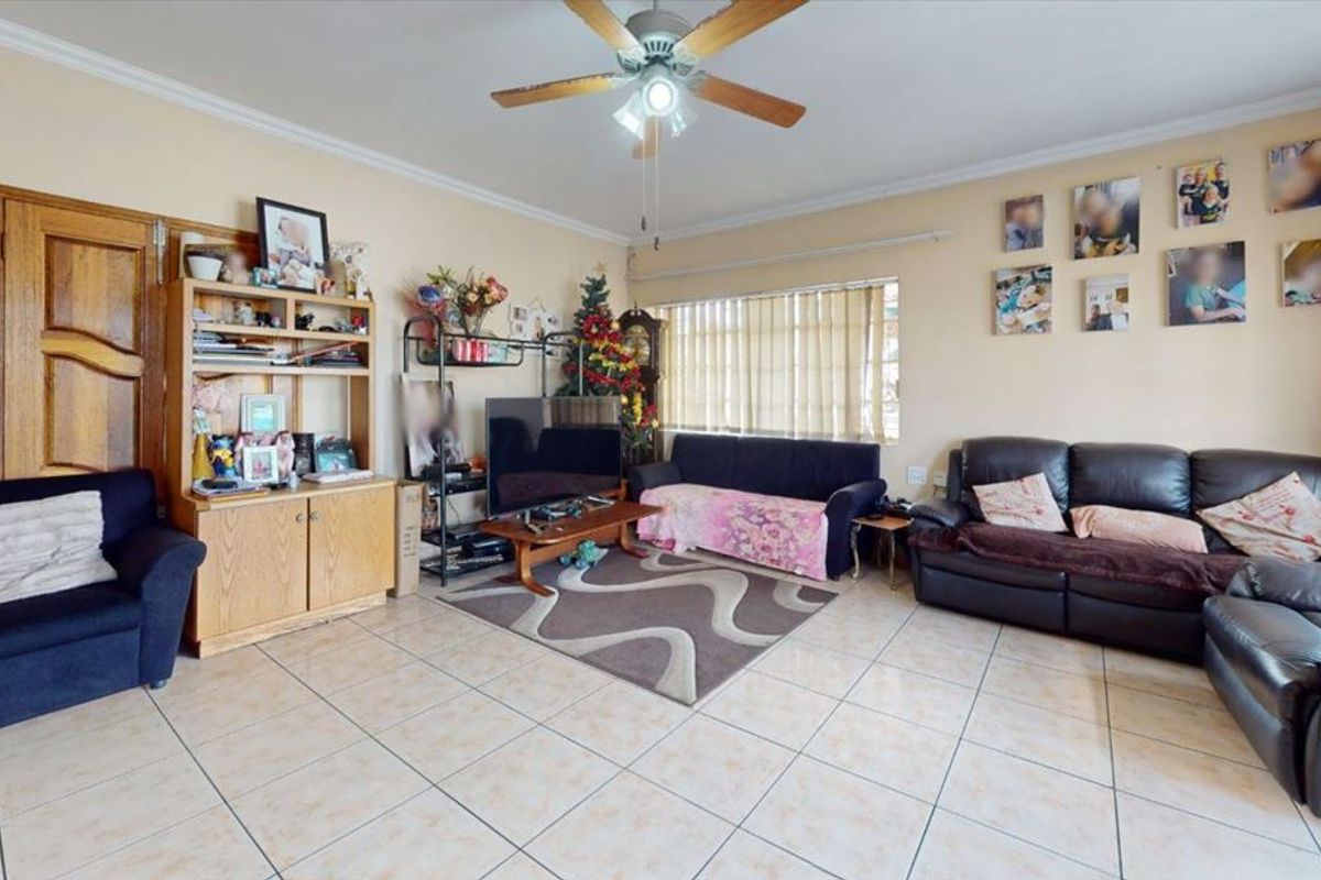 A spacious living room featuring tiled flooring, a ceiling fan, and coved cornicing, offering a functional layout with natural light from the window.