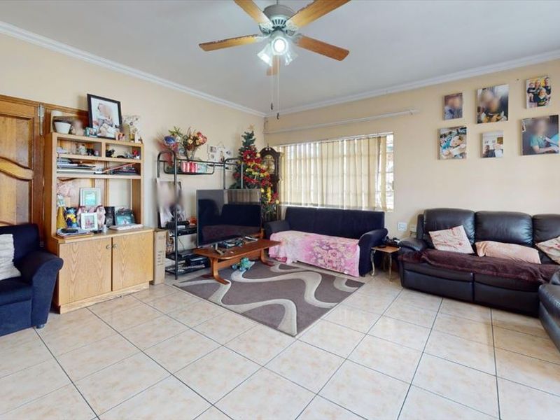 A spacious living room featuring tiled flooring, a ceiling fan, and coved cornicing, offering a functional layout with natural light from the window.
