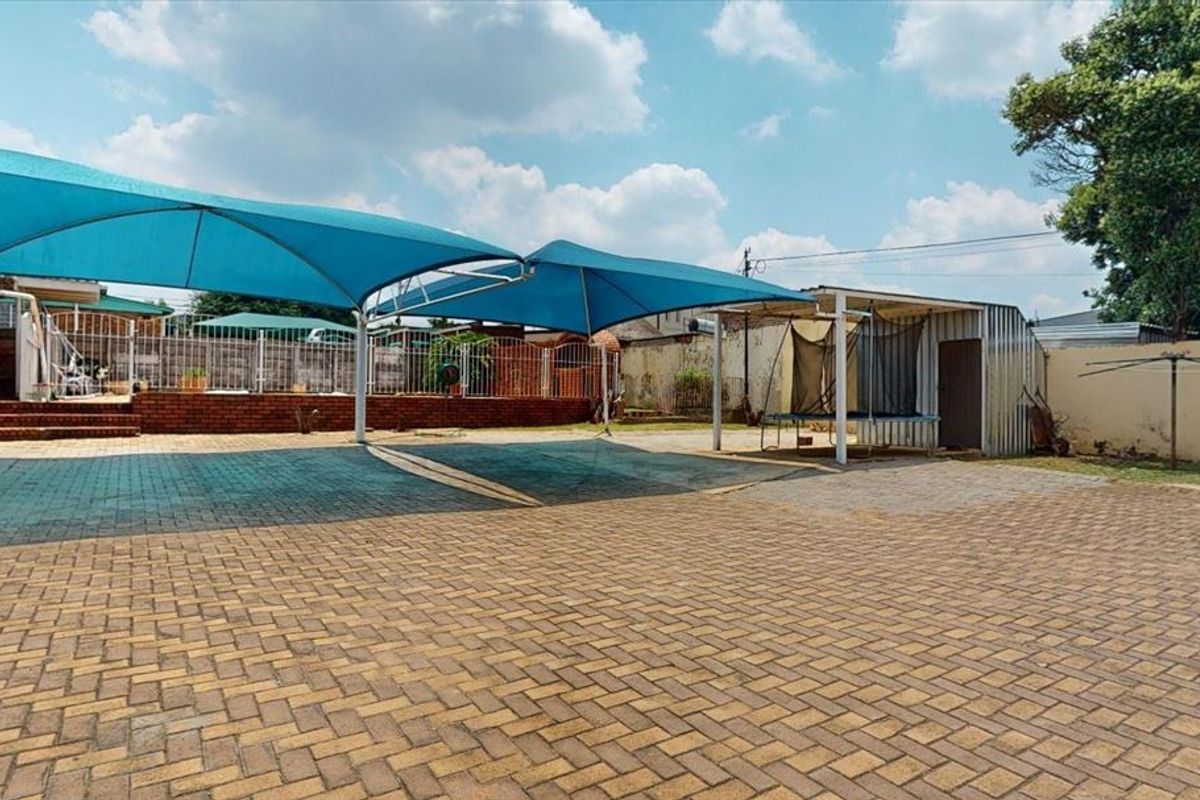 Spacious paved rear yard featuring a large shade sail structure, brick retaining walls, and a metal storage shed.