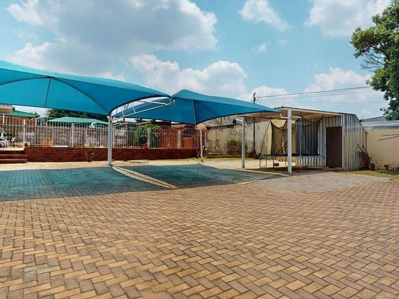 Spacious paved rear yard featuring a large shade sail structure, brick retaining walls, and a metal storage shed.