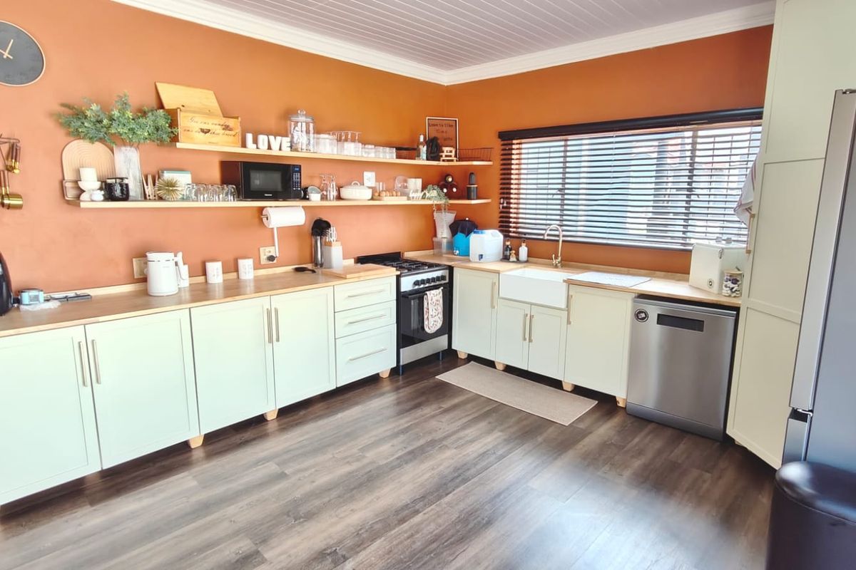 A functional kitchen featuring light-toned cabinetry, timber-look countertops, open shelving, a farmhouse sink, and a freestanding stove with dark wood-look flooring.