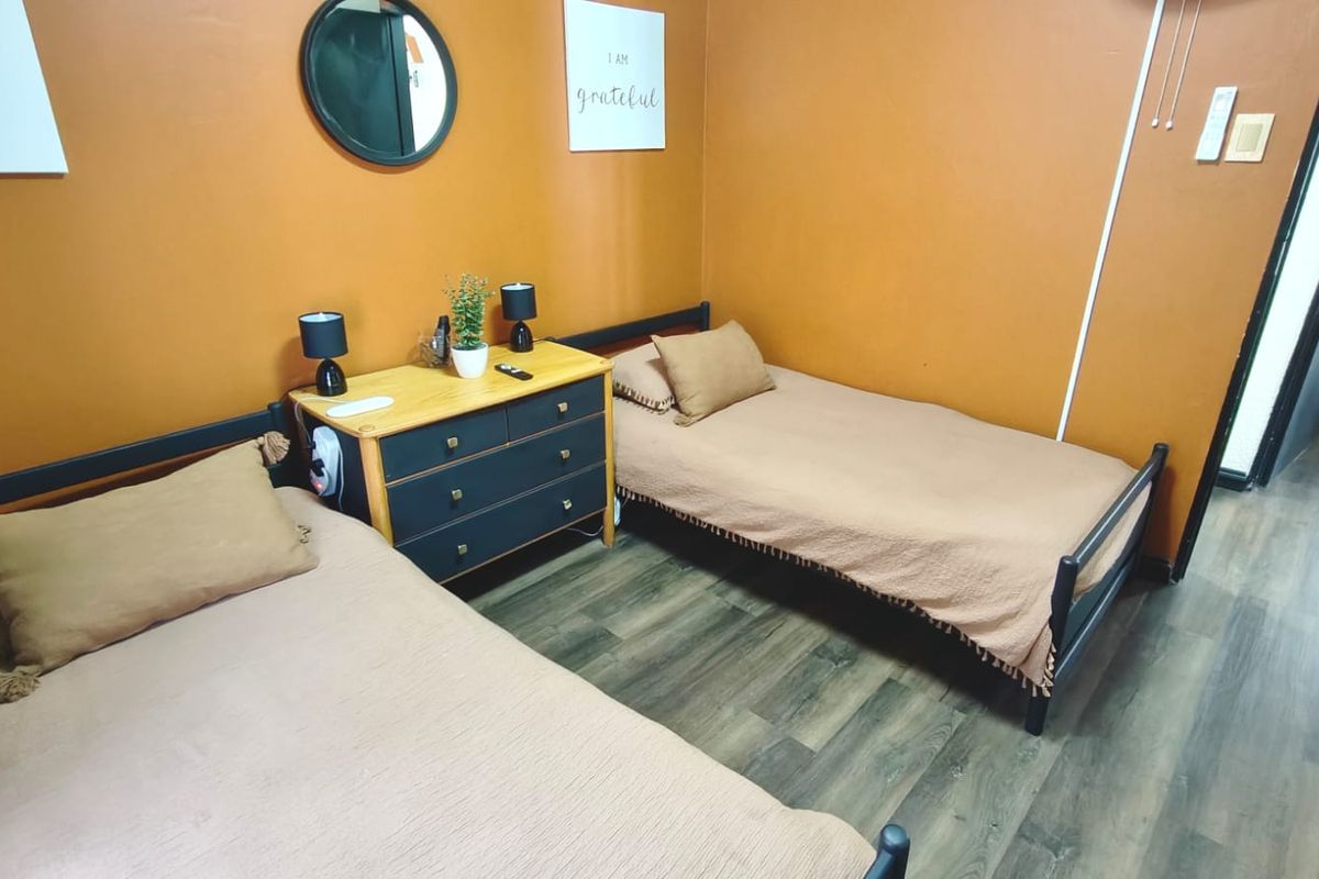 A bedroom featuring laminate flooring and painted walls, currently configured with two single beds and a central storage unit.