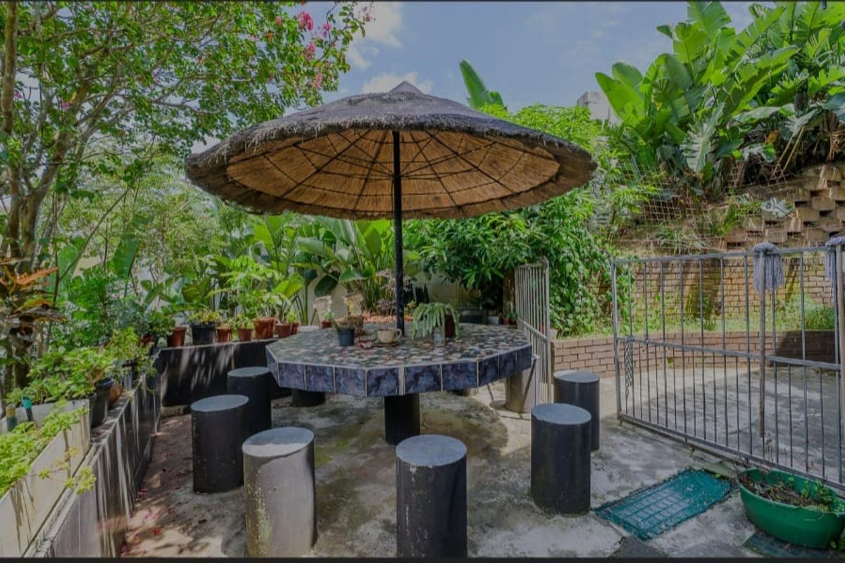 A private rear garden area featuring a built-in tiled table with a thatched umbrella, surrounded by established greenery and a brick retaining wall.