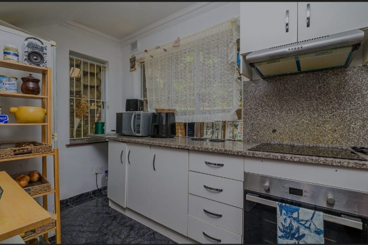 A functional kitchen featuring white cabinetry, granite countertops, a built-in oven, and an extractor fan, with tiled flooring and security bars on the window.