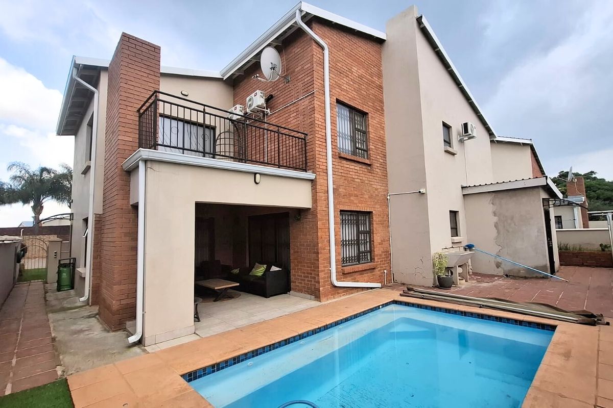 Rear view of a double-story brick house featuring a swimming pool, covered patio, and an upper-level balcony with metal railings.