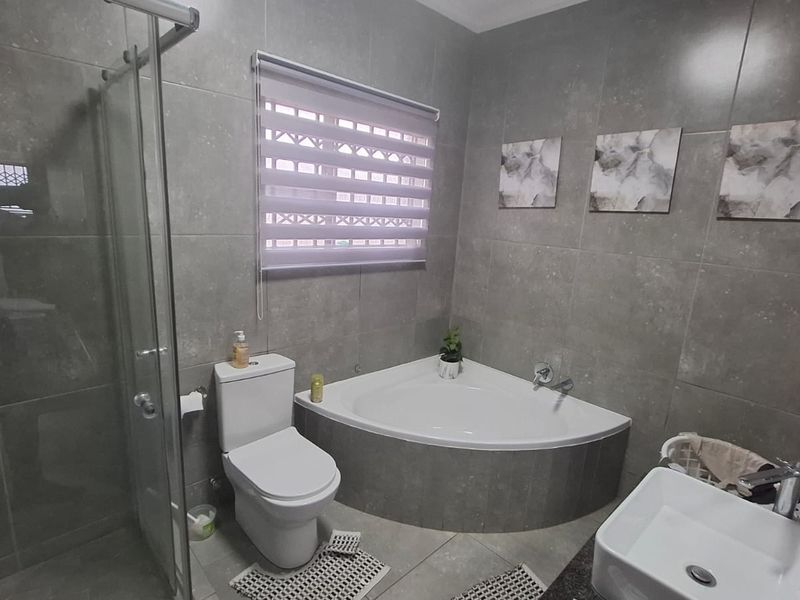 Modern bathroom featuring a corner bathtub, glass-enclosed shower, vessel sink, and contemporary grey wall and floor tiling.