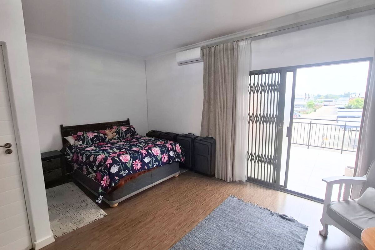Spacious bedroom featuring laminate flooring, a wall-mounted air conditioning unit, and direct access to a private balcony through a sliding glass door.