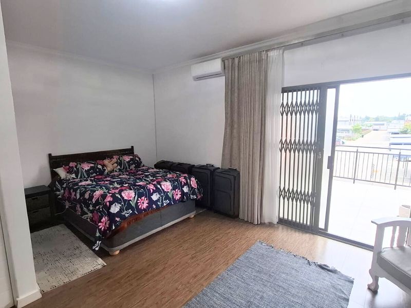 Spacious bedroom featuring laminate flooring, a wall-mounted air conditioning unit, and direct access to a private balcony through a sliding glass door.