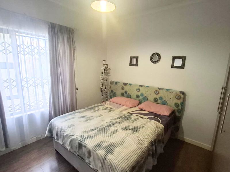 A functional bedroom featuring laminate flooring, a built-in wardrobe, and a window fitted with a security gate.