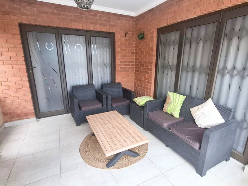 A covered patio area featuring exposed brick walls, light-colored floor tiles, and large aluminium-framed glass sliding doors providing access to the interior.