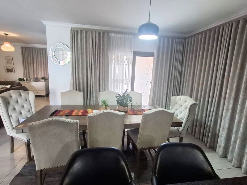 A well-lit dining area featuring tiled flooring, neutral curtains, and direct access to the exterior through a sliding glass door.