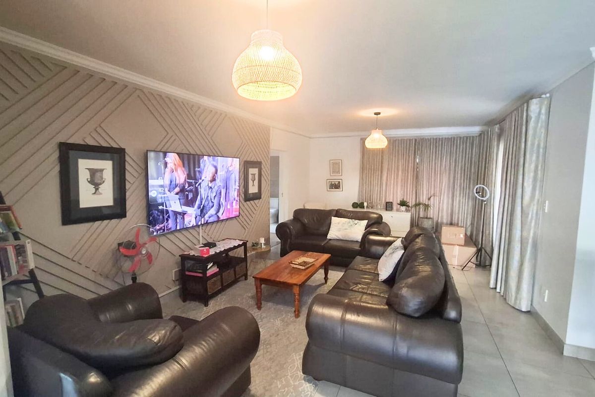 A comfortable living room featuring decorative wall paneling, tiled flooring, and neutral curtains, providing a functional and well-maintained space for relaxation.