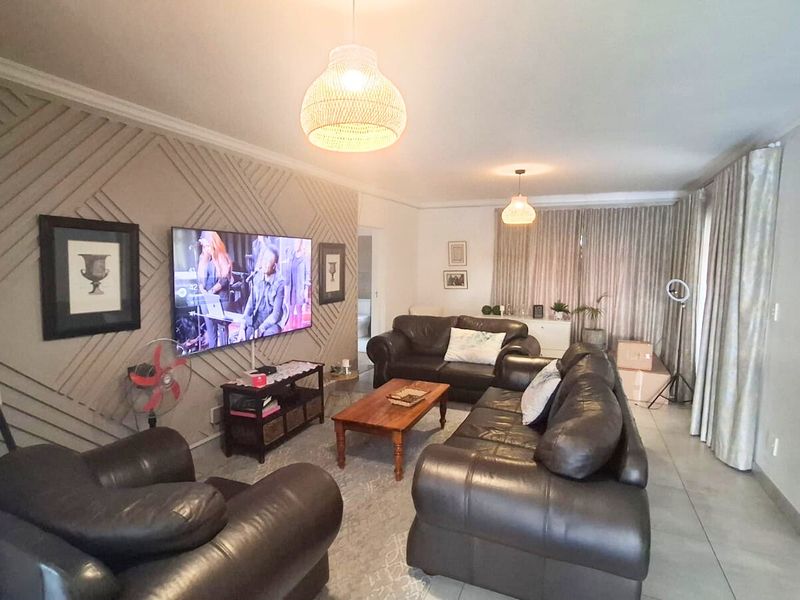 A comfortable living room featuring decorative wall paneling, tiled flooring, and neutral curtains, providing a functional and well-maintained space for relaxation.