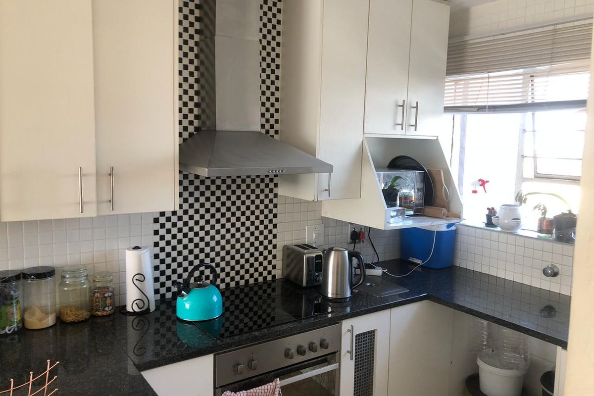 A functional kitchen featuring white cabinetry, dark granite countertops, a built-in electric oven and hob, and a distinctive checkered tile backsplash.