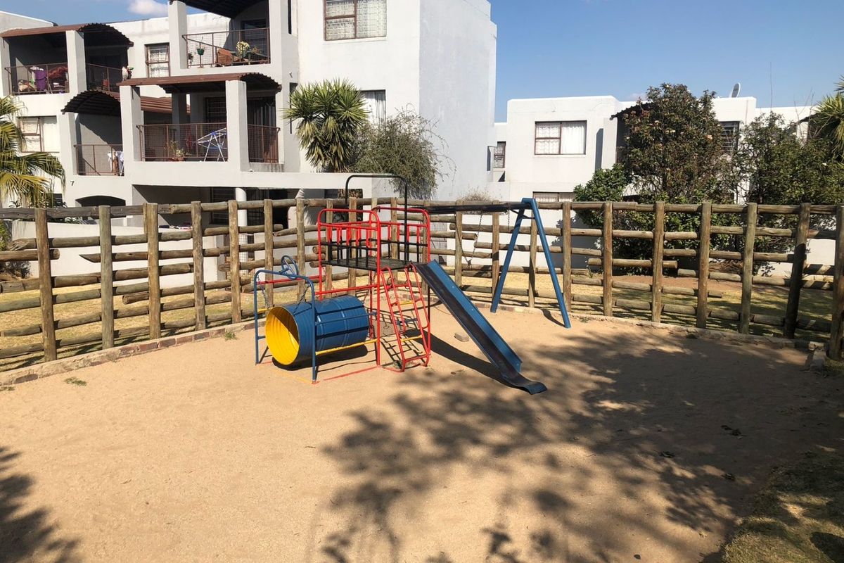 A communal outdoor area featuring a sand pit and playground equipment, enclosed by timber pole fencing within an apartment complex.