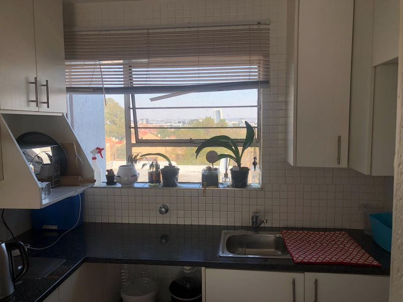 A functional kitchen featuring dark laminate countertops, white cabinetry, a stainless steel sink, and a tiled backsplash with a window view.