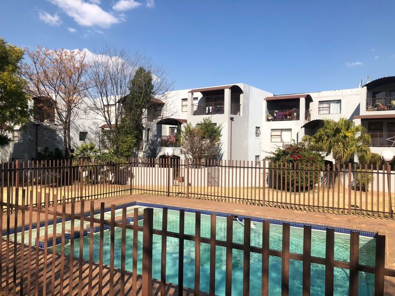 A communal swimming pool area featuring metal safety fencing and paved surrounds, set against the backdrop of a multi-story apartment complex.