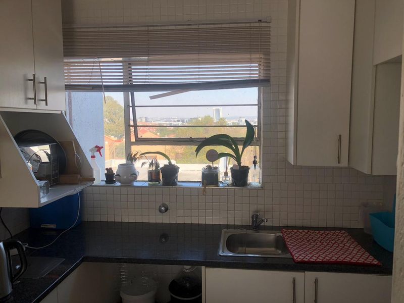 A functional kitchen featuring dark laminate countertops, white cabinetry, a stainless steel sink, and a window with security bars and city views.