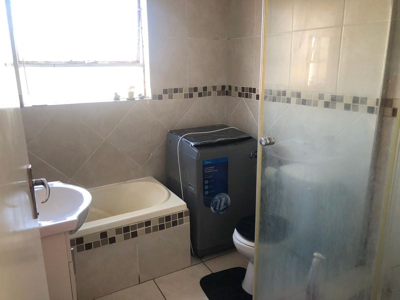 A functional bathroom featuring a built-in bathtub, a separate glass-enclosed shower, a pedestal basin, and neutral ceramic tiling throughout.