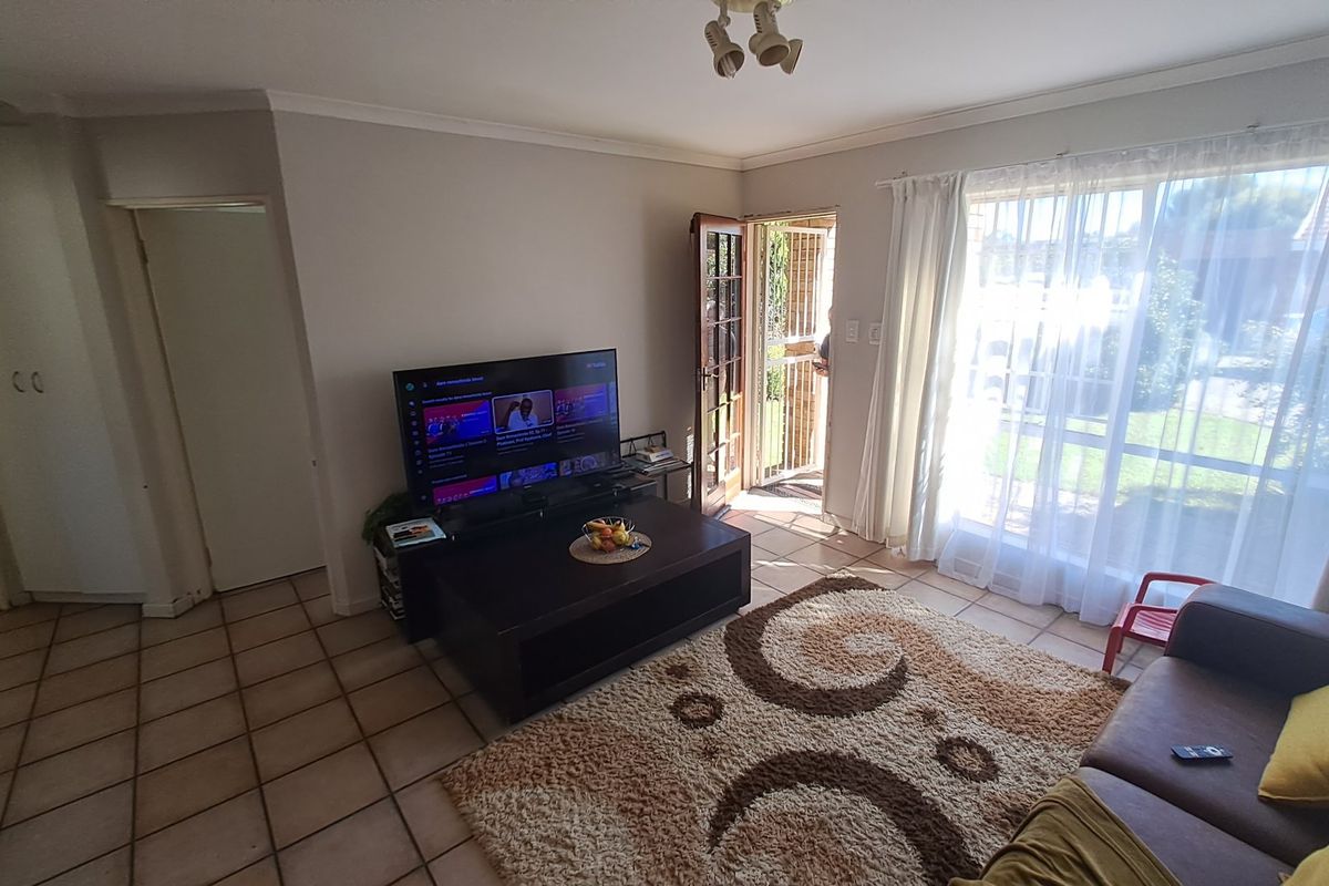 A living room featuring tiled flooring, large windows providing natural light, and direct access to an outdoor area through a security gate.