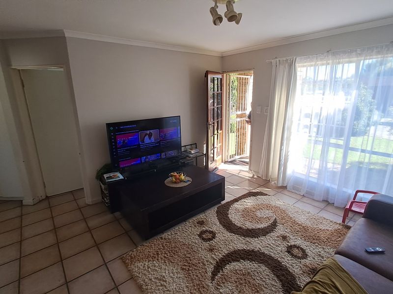A living room featuring tiled flooring, large windows providing natural light, and direct access to an outdoor area through a security gate.