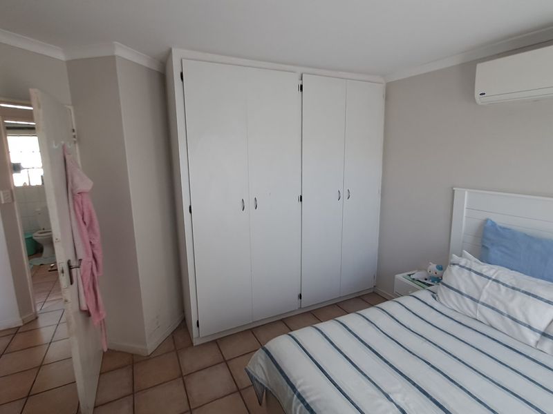 A bedroom featuring built-in cupboards, a wall-mounted air conditioning unit, and tiled flooring, with an adjacent view into a bathroom.