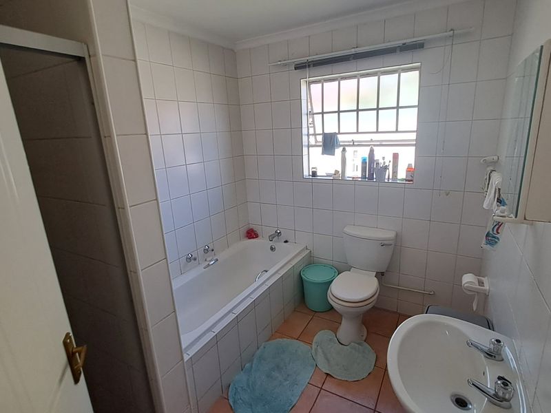A functional bathroom featuring a built-in bathtub, pedestal basin, and toilet with tiled walls and flooring.