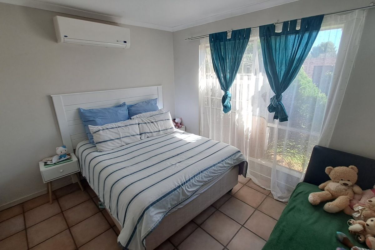 A bedroom featuring tiled flooring, a wall-mounted air conditioning unit, and large windows allowing natural light.