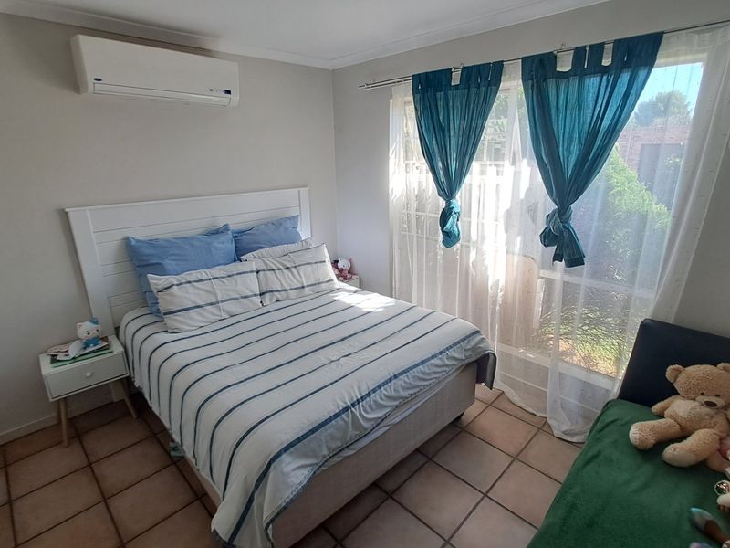 A bedroom featuring tiled flooring, a wall-mounted air conditioning unit, and large windows allowing natural light.