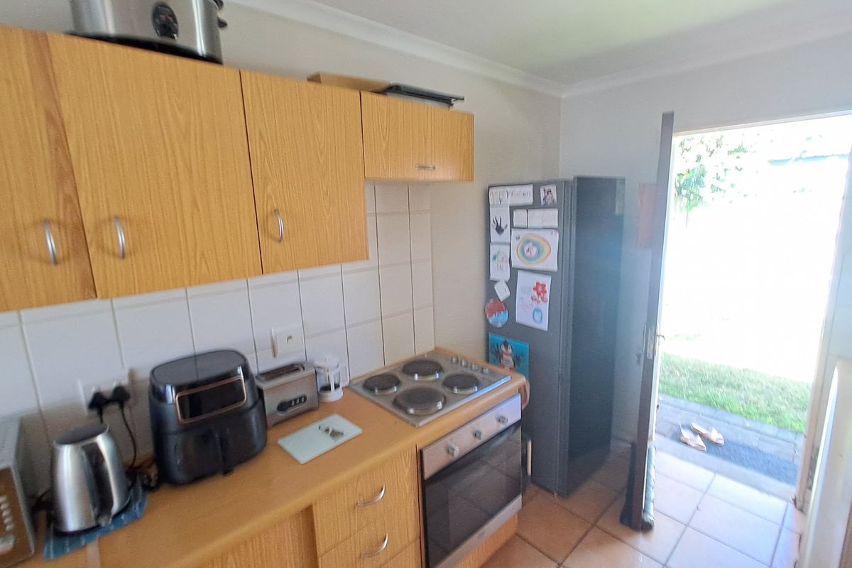 A functional kitchen featuring wood-look cabinetry, tiled splashbacks, a built-in electric oven and hob, with direct access to the rear garden.