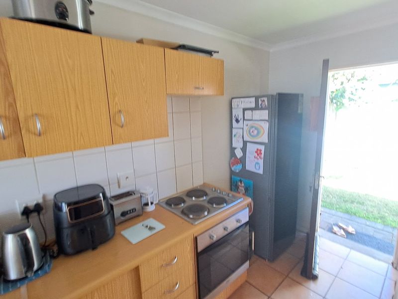 A functional kitchen featuring wood-look cabinetry, tiled splashbacks, a built-in electric oven and hob, with direct access to the rear garden.