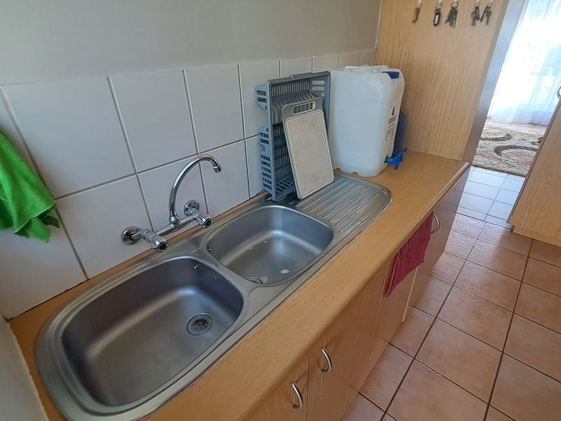 A functional scullery area featuring a double stainless steel sink, laminate countertop, and tiled splashback, providing practical utility space.