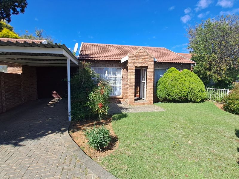 Front view of a townhouse featuring a face-brick facade, tiled roof, paved driveway, covered carport, and a well-maintained front garden.