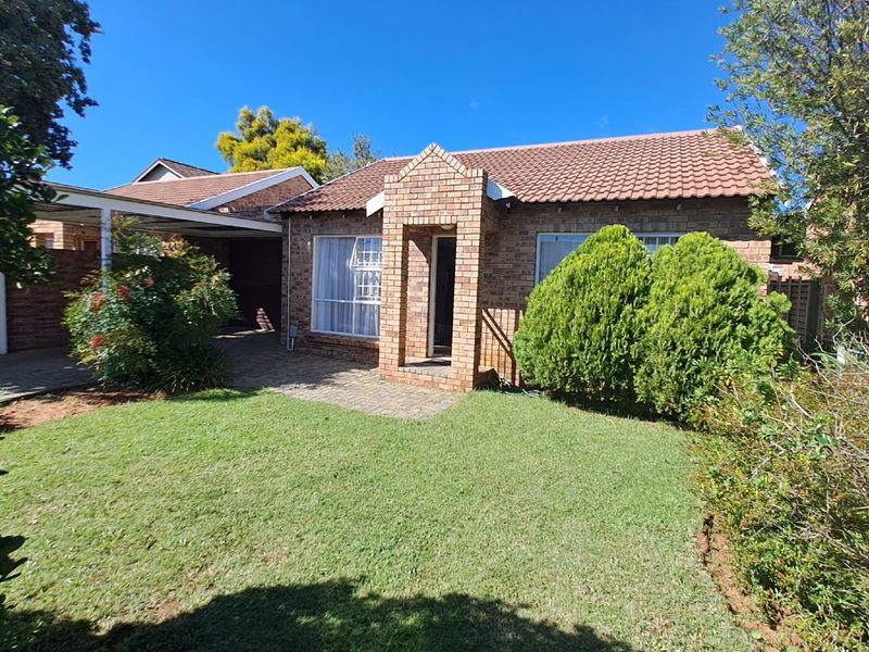 Front view of a face-brick townhouse featuring a tiled roof, covered carport, and a well-maintained front garden with established landscaping.