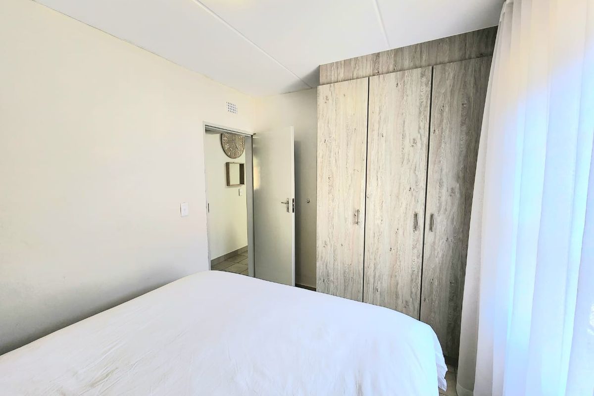 A bedroom featuring built-in wood-look cupboards, tiled flooring, and a neutral color palette, offering a functional and tidy living space.