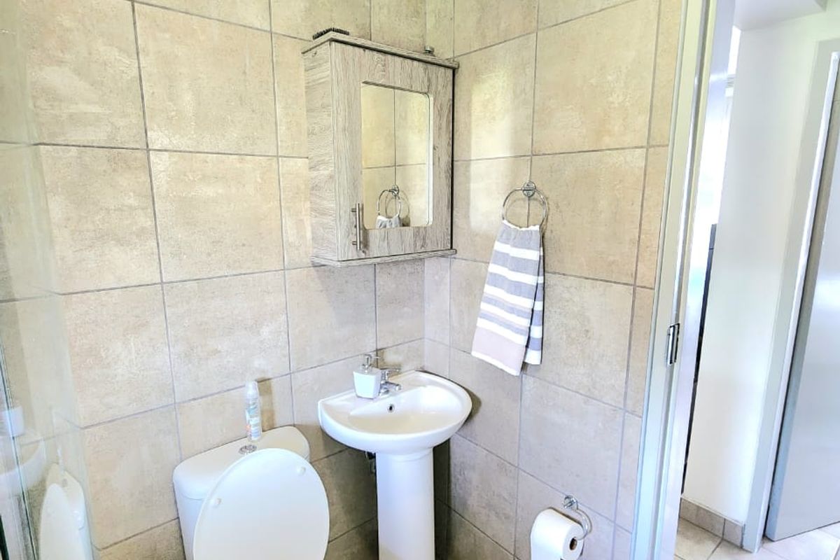 A functional bathroom featuring a pedestal basin, toilet, and shower enclosure with neutral ceramic wall and floor tiling.