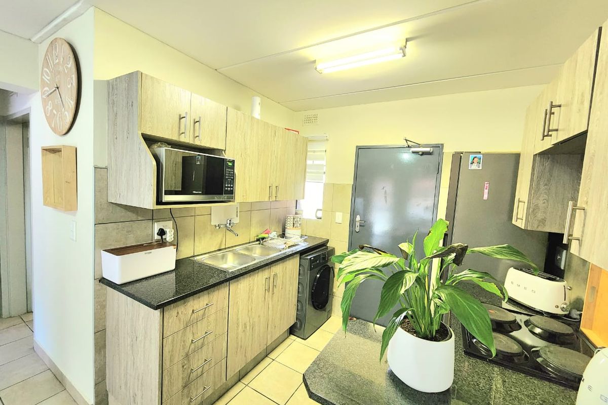 A functional kitchen featuring light wood-look cabinetry, granite countertops, a double basin sink, and integrated appliances, finished with ceramic floor tiles.